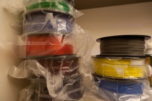 Colorful spools of filament, which the printer uses to construct the objects, are stacked in the corner awaiting use.