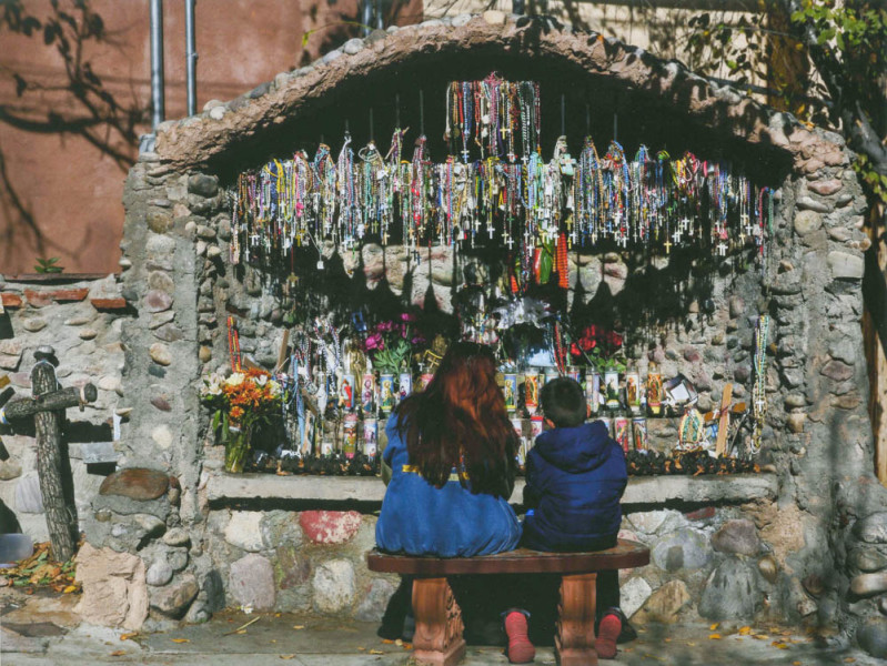 Two visitors sitting in front of a rosary decorated shrine in the El Santuario de Chimayo in Chimayo, NM. Photo by Eduardo Rocha.