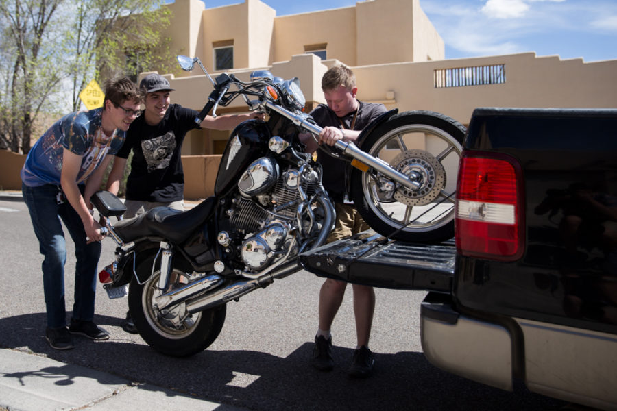 Aiden Willink and Derek Conkins help Ambrose Taylor lift his motorcycle into the Back of a truck to take back to campus. Photo by Jason Stilgebouer