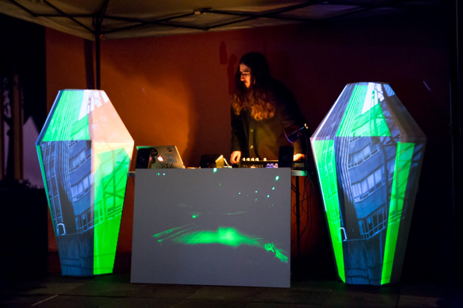 A Dj mixes music next Video mapping display at outdoor vision festival. Photo by Jason Stilgebouer